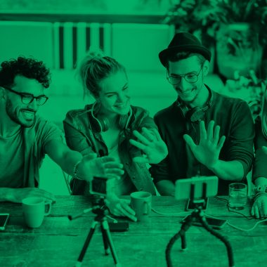 4 young adults sitting at a table in a cafe and smiling at a camera phone, green filter.